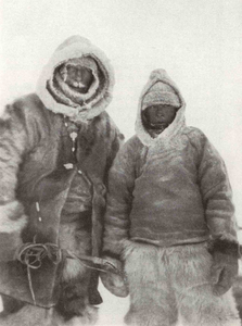 Alfred Wegener und eine weitere Person stehen nebeneinander. Sie tragen dicke Kleidung mit Kapuzen aus Pelz. 